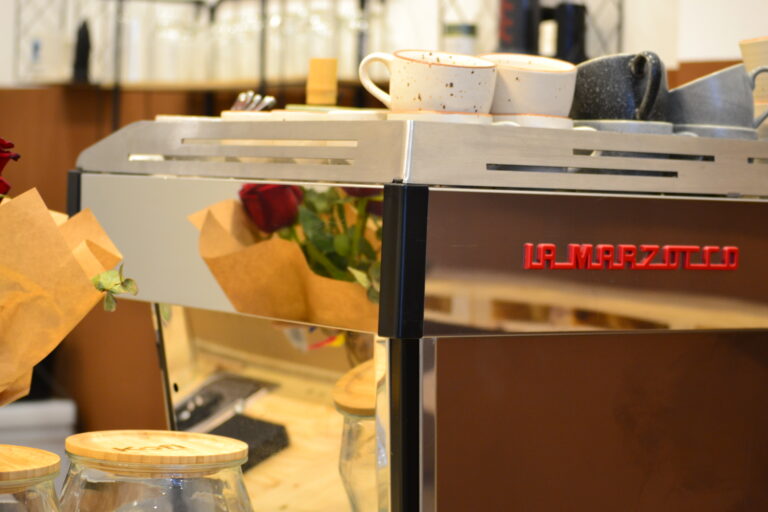 Una màquina de cafè La marzocco amb tasses i accessoris sobre una taula de fusta a la cafeteria Kofi