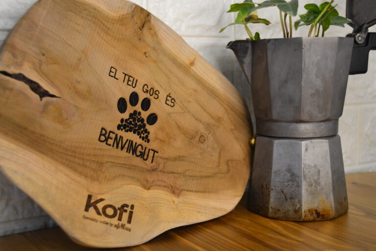 Una fusta gravada amb el texte El teu gos és benvingut penjada a la porta de la cafeteria Kofi