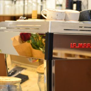 Una màquina de cafè La marzocco amb tasses i accessoris sobre una taula de fusta a la cafeteria Kofi